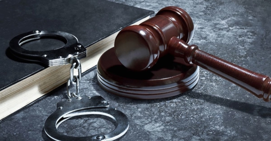 handcuffs and judge gavel with book on asphalt ground